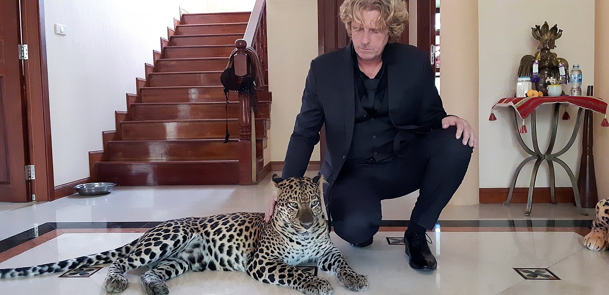 Man in a Suit in a Fancy House Squatting Down and Petting a Leaopard