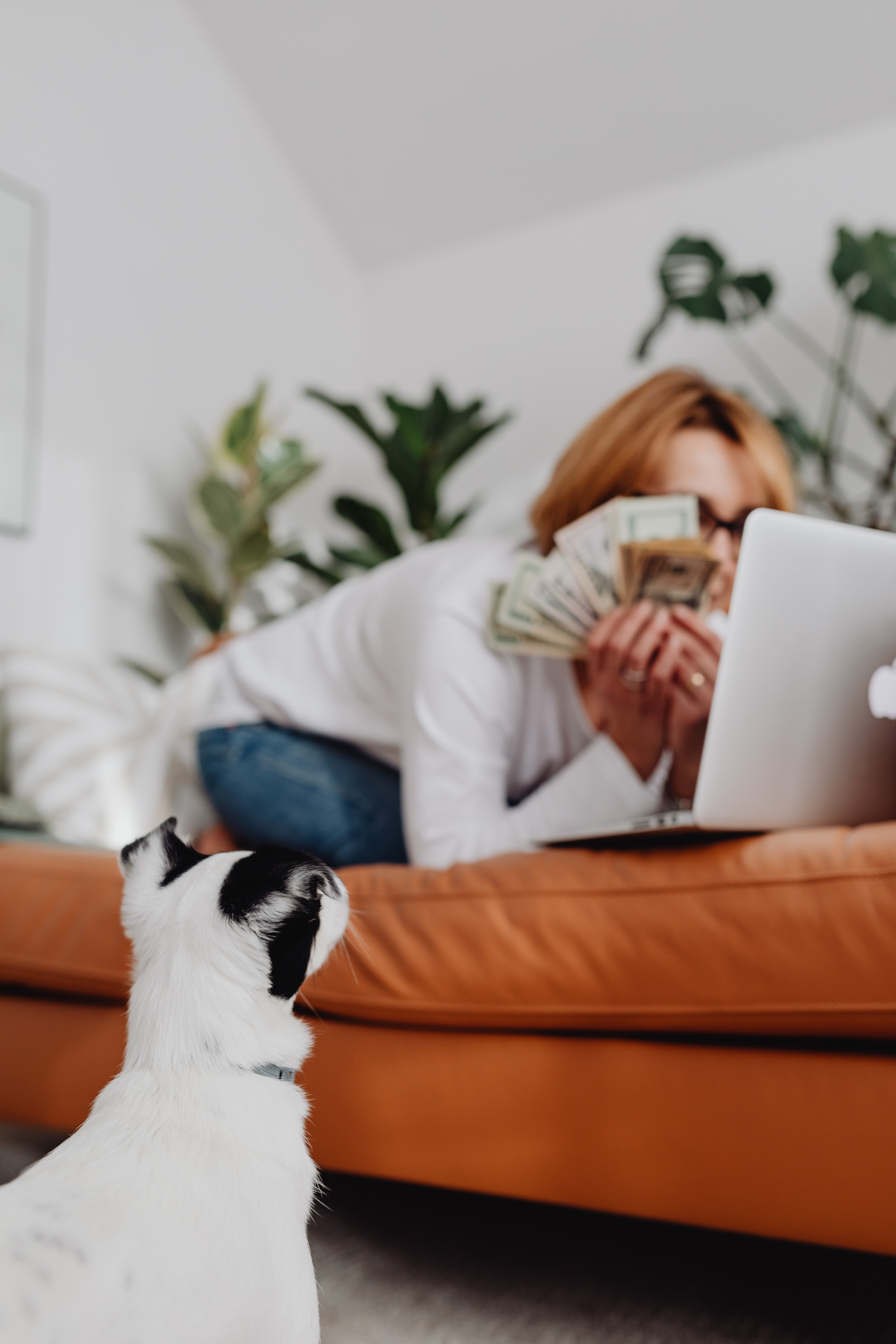 Woman Laying on a Couch With Lots of Money in her Hands and a Cat is on the Floor Looking at Her