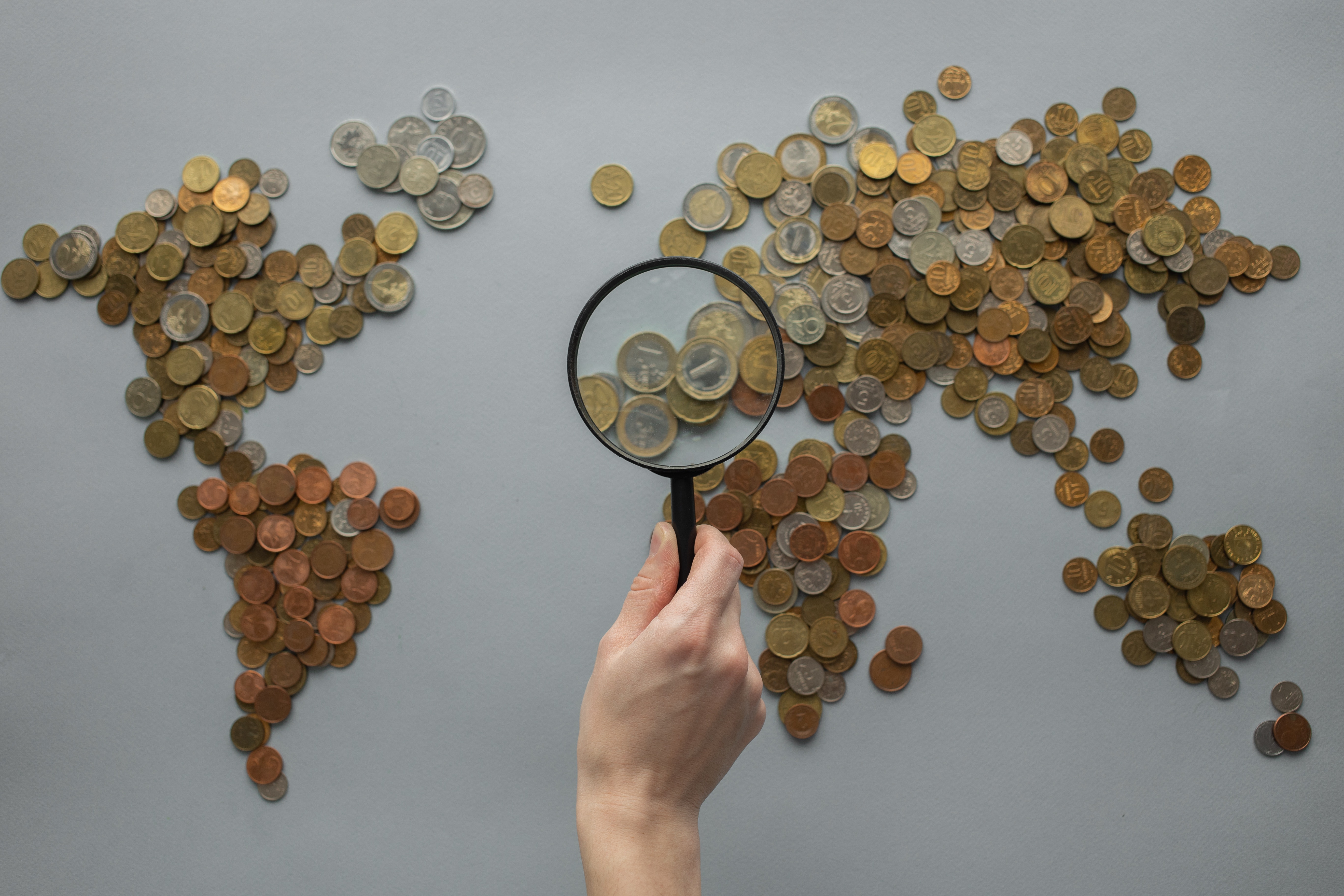 Coins Arranged Like a Map of the World. There is a Person Holding a Magnifying Glass in Front of It, Highlighting the Economic Benefits of Ecotourism Coins Arranged Like a Map of the World. There is a Person Holding a Magnifying Glass in Front of It, Highlighting the Economic Benefits of Ecotourism