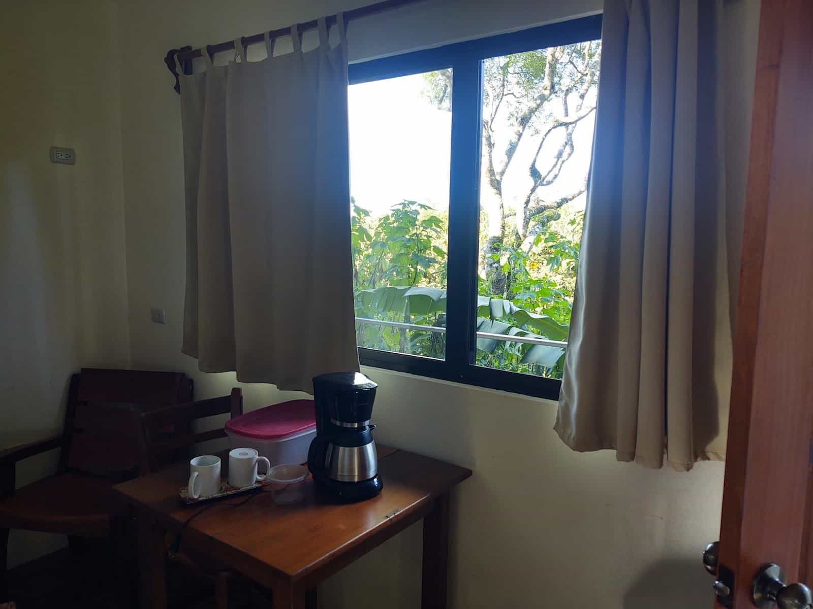 Another View of Our Room in Valle Escondido. This Is Looking out a Large Window. There Is a Coffee Maker, Two Cups, and a Tupperware Container on a Table.